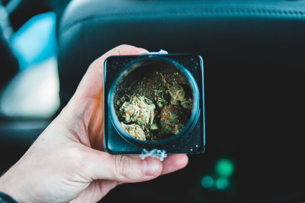 Hand holding square black flower jar with cannabis inside