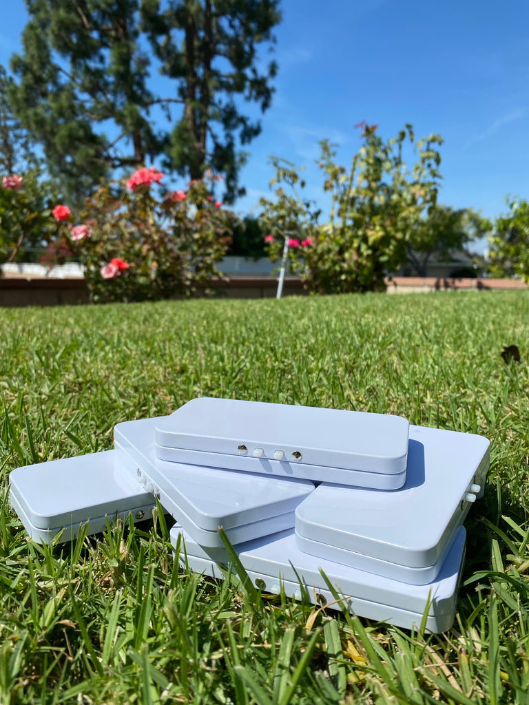 White Tin Boxes stacked on top of each other on top of grass with flowers, trees, and blue sky in background